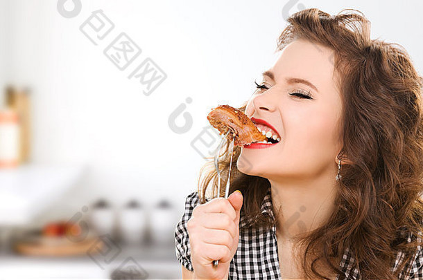 饿了年轻的女人吃肉叉厨房
