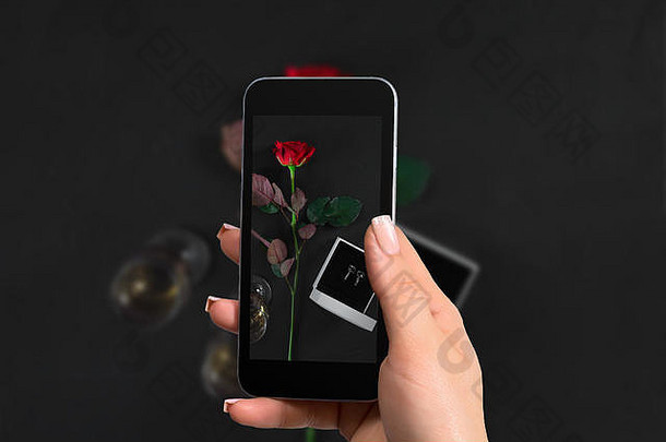 女手智能手机使照片黑暗红色的玫瑰盒子耳环黑色的背景