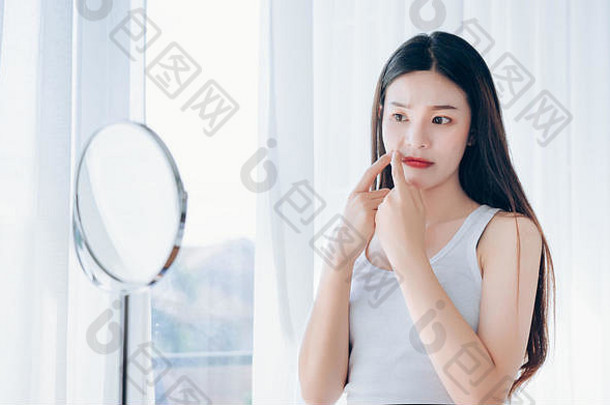 年轻的亚洲女人挤压痤疮问题脸镜子护肤品