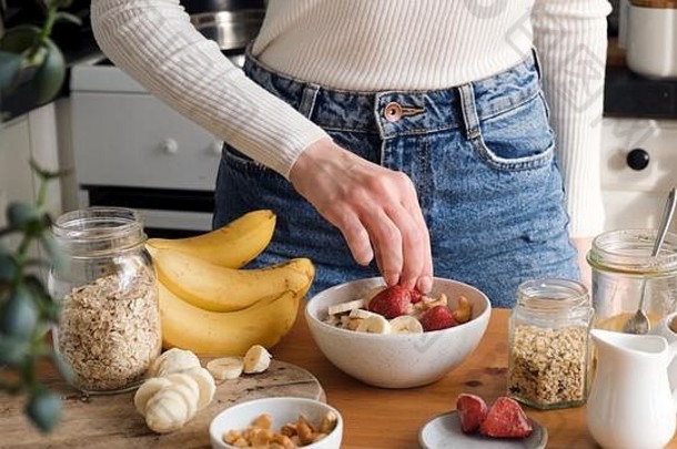 添加水果早餐燕麦片粥碗女人准备健康的早餐厨房概念健康的吃生活方式