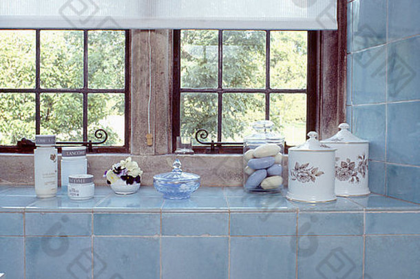 关闭化妆品陶器罐子柔和的蓝色的平铺的窗台上白色盲目的浴室