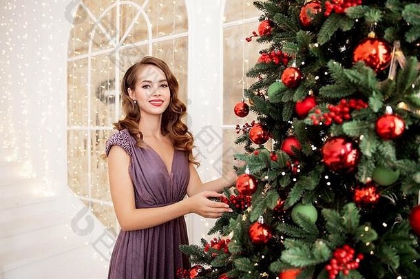 美丽的女孩晚上衣服化妆发型装修圣诞节树红色的球快乐微笑