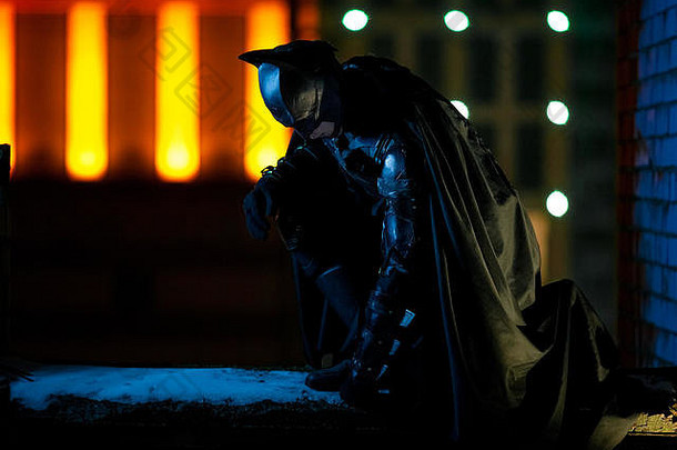 男人。穿着面具头盔护甲黑色的斗篷坐在背景晚上城市灯建筑动漫真人秀