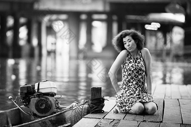 美丽的年轻的亚洲女人坐在木河码头黑白照片