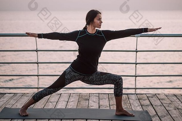年轻的浅黑肤色的女人女人瑜伽练习木海路堤早....女孩黑色的体育服装伸展运动实践健康的