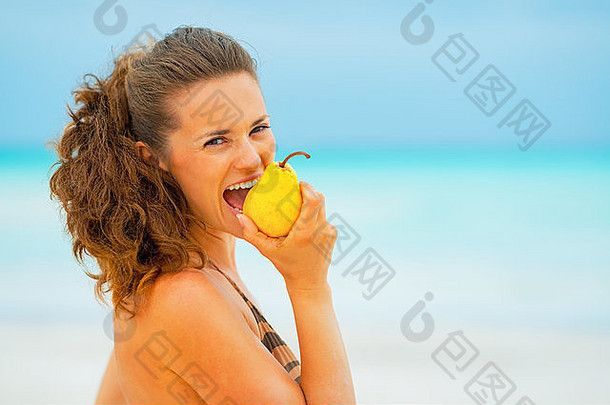 肖像年轻的女人吃梨海滩