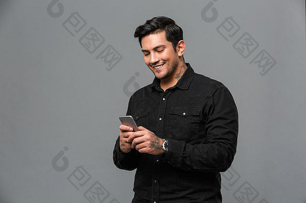 图像快乐的年轻的英俊的男人。站孤立的灰色墙聊天移动电话
