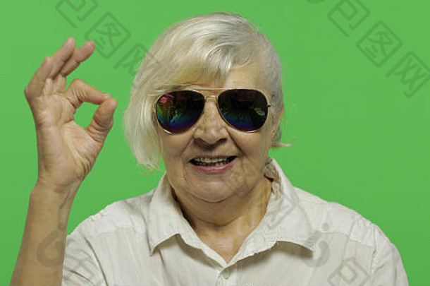 上了年纪的女人太阳镜显示手势微笑漂亮的祖母白色衬衫的地方标志文本浓度关键绿色屏幕背景