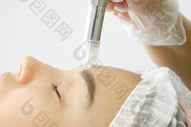 美容师手移动磨皮设备年轻的女人额头白色诊所墙极端的关闭视图