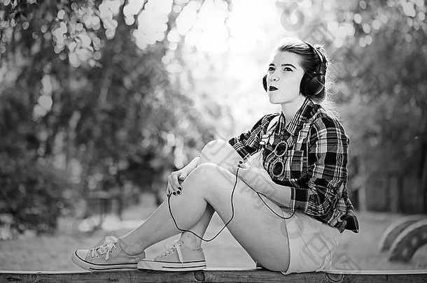 年轻的赶时髦的人女孩听音乐耳机夏天公园黑色的白色照片概念快乐的青年