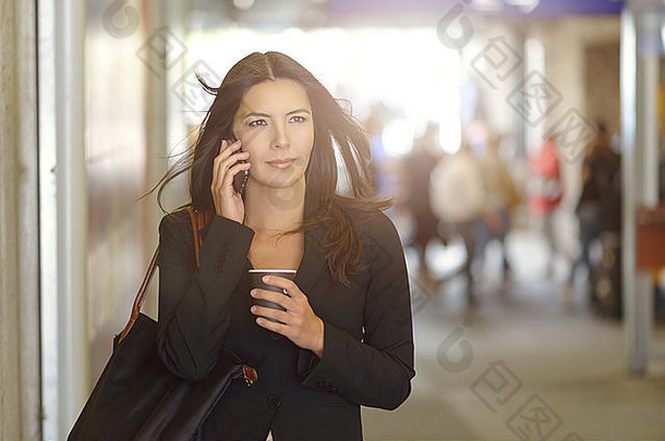 有吸引力的年轻的女商人调用移动电话走内部购物中心持有杯咖啡