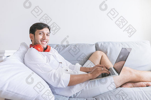 年轻的男人。放松沙发上移动PC耳机一边视图英俊的男人。移动PC<strong>相机</strong>微笑西蒂