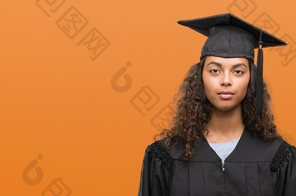年轻的拉美裔女人穿毕业统一的自信表达式聪明的脸思考