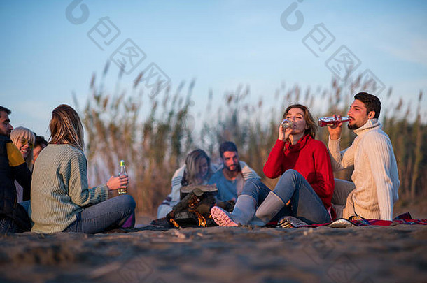 年轻的夫妇享受朋友篝火海滩日落喝啤酒