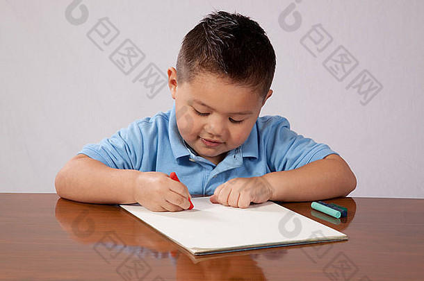 可爱的年轻的男孩坐着木表格纸铅笔写作画纸