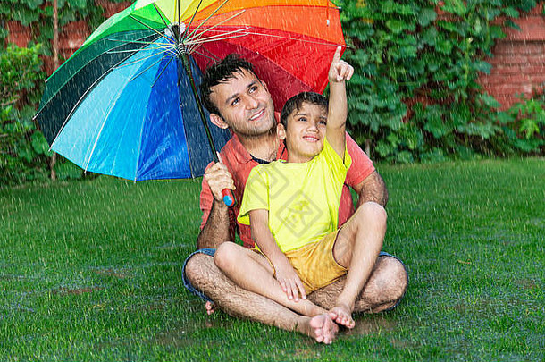 幸福的家庭父亲孩子男孩sitting-on-grass伞指出灰尘雨在户外的花园