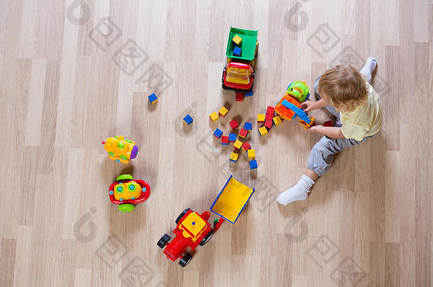金发碧眼的孩子男孩玩色彩斑斓的车玩具地板上前视图
