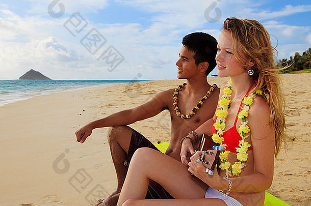 夏威夷男人。高加索人金发碧眼的女孩坐冲浪板海滩玩尤克里里琴
