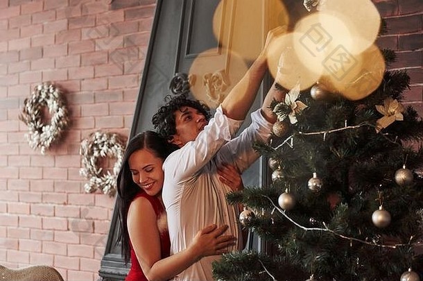 女孩拥抱的男朋友爱浪漫的夫妇沙拉酱圣诞节树房间棕色（的）墙壁炉