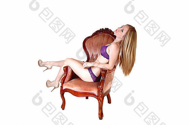 年轻的漂亮的女人内衣坐着粉红色的扶手椅腿一边长金发碧眼的头发挂