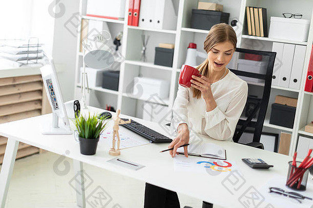 年轻的女孩坐着表格办公室持有红色的杯手采取表图表表格