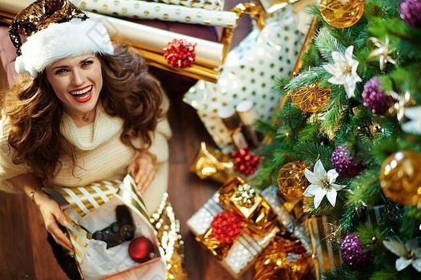 上视图快乐时尚的女人长浅黑肤色的女人头发黄金金片裙子白色毛衣装饰圣诞节树现在盒子包装
