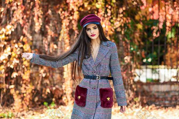 年轻的美丽的女孩穿冬天外套帽秋天叶子背景