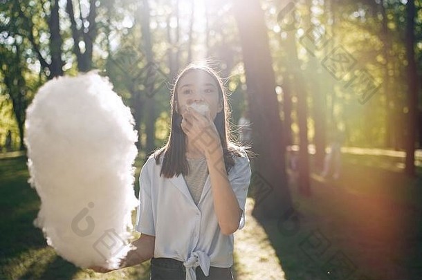 肖像漂亮的年轻的女孩吃棉花糖果公园