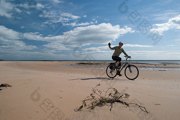 女人骑自行车挥舞着海滩比德内尔湾诺森伯兰郡英格兰阳光明媚的一天