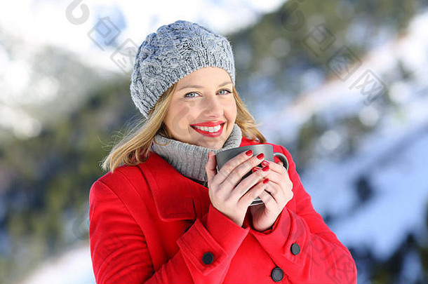肖像时尚快乐女人穿红色的外套摆姿势持有咖啡杯子雪山冬天
