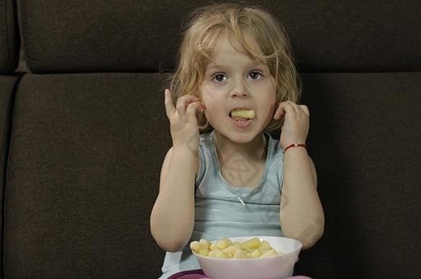 美丽的金发女郎女孩坐着沙发首页吃玉米泡芙可爱的孩子味道puffcorns内部儿童餐