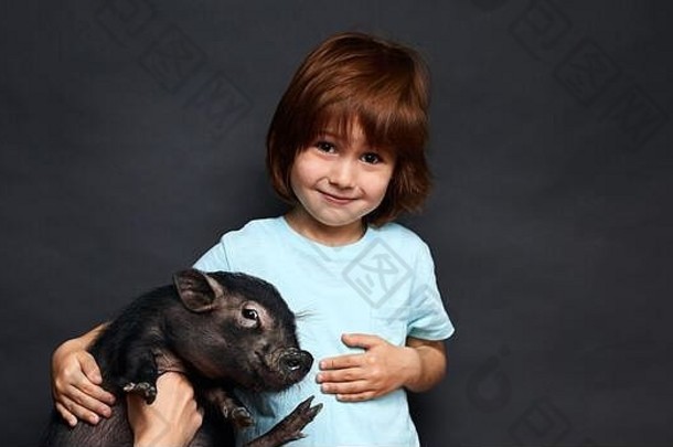 可爱的红发男孩相机无辜的微笑持有最喜欢的宠物黑色的小猪孤立的黑色的背景