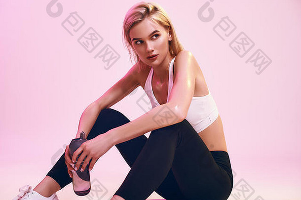 放松锻炼可爱的年轻的金发女郎女人体育服装持有瓶水放松坐着地板上粉红色的背景工作室体育运动活跃的生活方式