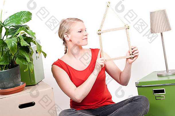 年轻的女人折叠规则房子象征坐在移动纸板植物