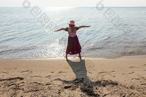 年轻的女人孩子他可爱的夏天衣服使手势提高了手海海岸浅水