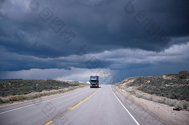 黑暗灰色的半卡车预告片接近相反车道水平长路背景狂风暴雨的天空内华达