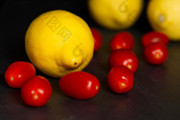 黄色的柠檬红色的婴儿李子西红柿孤立的黑暗背景板岩表面水果健康的吃概念
