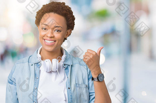 年轻的非洲美国女人穿耳机孤立的背景微笑快乐脸指出一边拇指