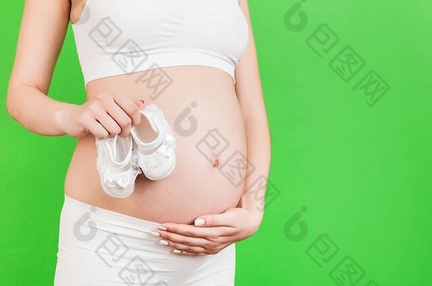 裁剪图像怀孕了女人白色内衣持有婴儿女孩靴肚子绿色背景快乐怀孕复制空间