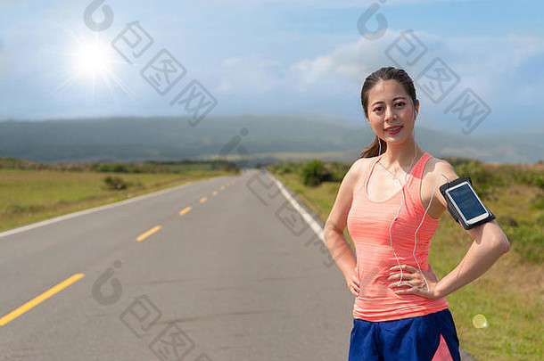 专业女慢跑者穿体育服装站路街自信移动电话听歌曲阳光明媚的背景