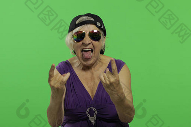 上了年纪的女人呼喊微笑显示舌头漂亮的快乐祖母太阳镜帽的地方标志文本浓度关键绿色屏幕背景