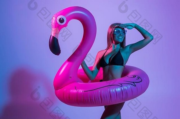 肖像年轻的女人穿着泳衣摆姿势充气火烈鸟孤立的粉红色的背景