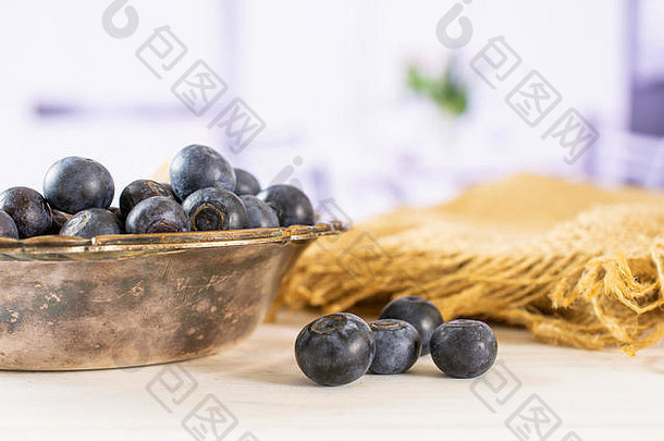 很多新鲜的甜蜜的紫色的蓝莓美国铁碗黄麻布红色的花白色背景