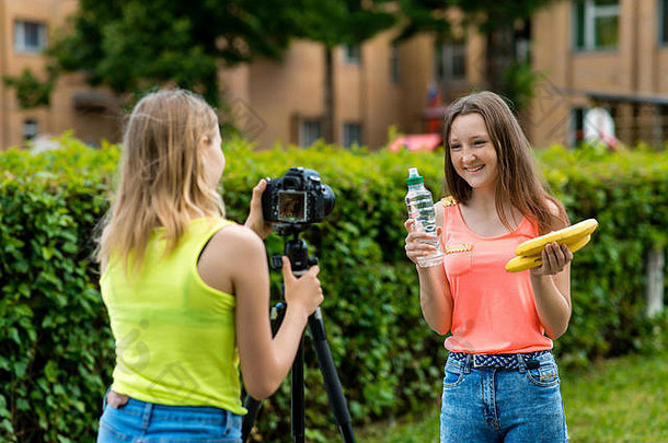 女孩女朋友夏天公园记录视频相机健康的饮食手持有香蕉瓶水幸福的幸福的微笑