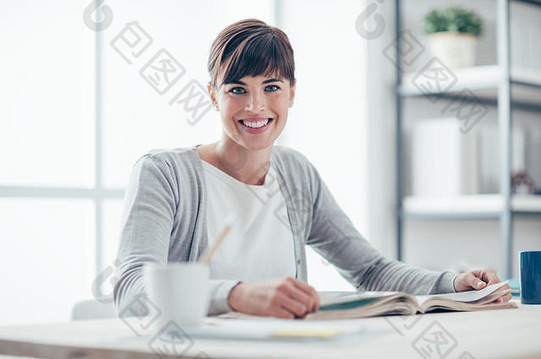 微笑年轻的女人坐着桌子上放松阅读书学习教育概念