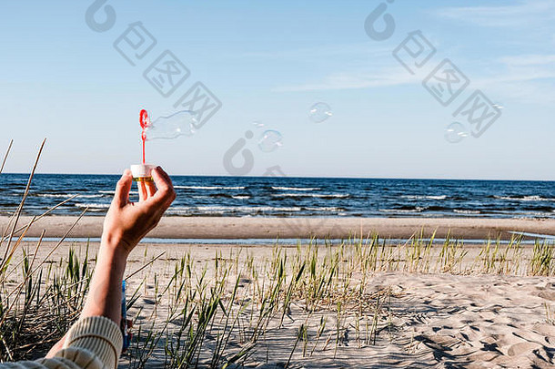 手年轻的女玩肥皂泡沫在户外海滩吹风