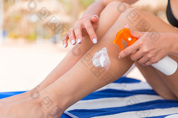 女孩坐着日光浴浴床应用太阳奶油腿海滩