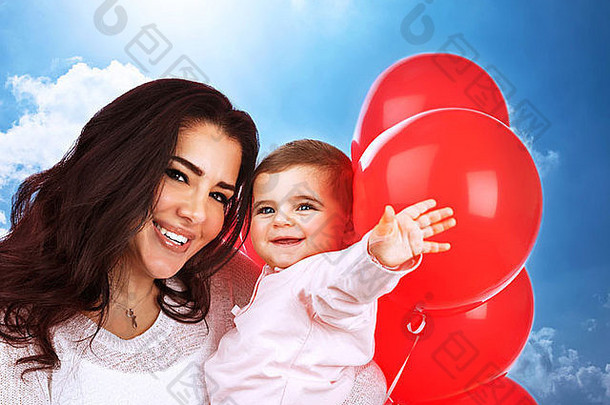 特写镜头肖像可爱的快乐的妈妈。携带甜蜜的婴儿女儿有趣的在户外玩红色的气球快乐家庭