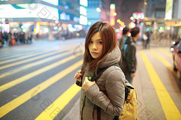 美丽的年轻的女孩站看晚上在香港香港失去了城市忙人群黄色的斑马穿越模糊背景
