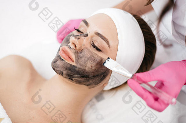 放松美丽的女人自然<strong>化妆水</strong>疗中心沙龙手美容师应用黑色的面具脸刷